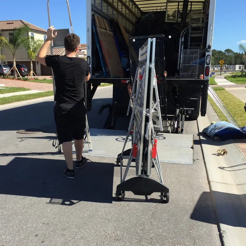 A mover loading a large flat item at the lift gate of a box truck.
